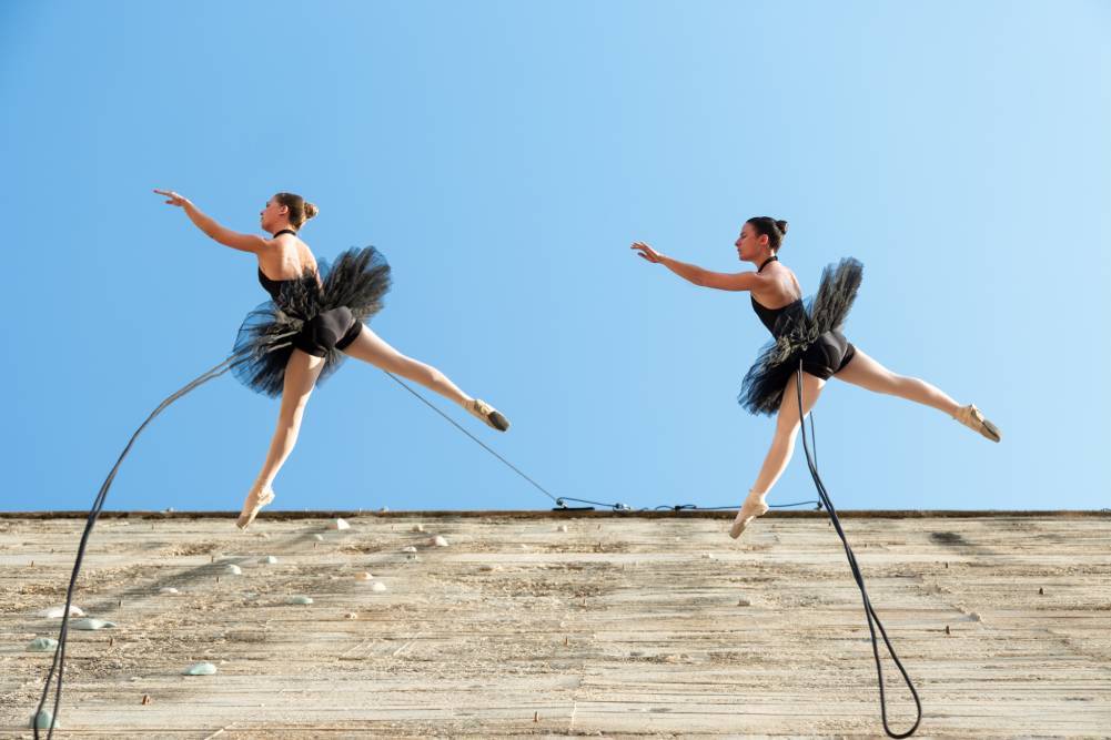 Two ballerinas perform while suspended from a building