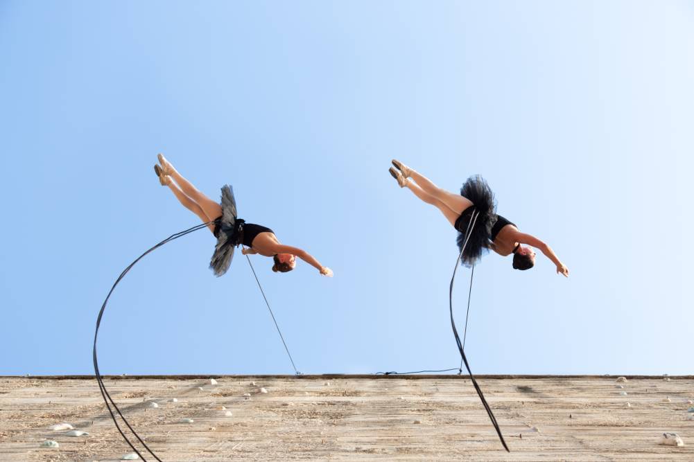 Two ballerinas perform while suspended from a building