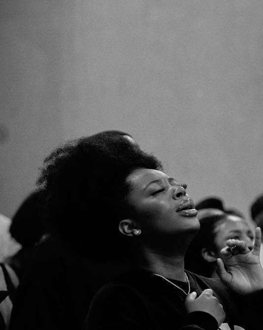 Black and white photograph shows woman raising her head with eyes closed in prayer