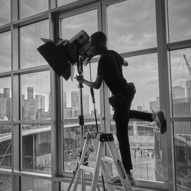 A student balances on a stepladder to adjust studio lights